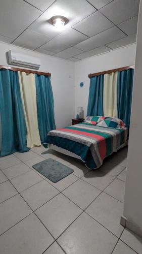 a bedroom with a bed with blue curtains and a tiled floor at La casa de don Matilde in San Pedro Sula