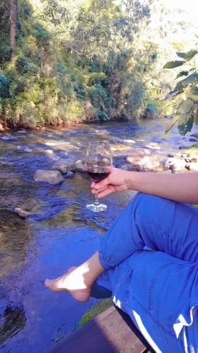 a person holding a glass of wine next to a river at Pousada Bosque do Visconde in Visconde De Maua