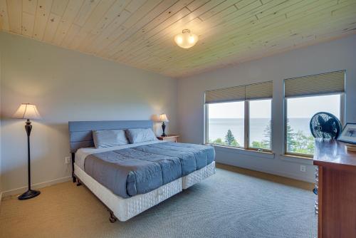 a bedroom with a bed with a blue bedspread and two windows at Tofte Tranquility Lakefront Townhome with Balcony! in Tofte