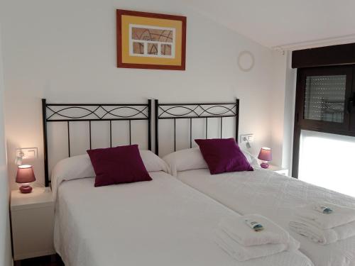 a bedroom with two white beds with purple pillows at Apartamentos La Piedra de Nájera in Nájera