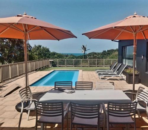 a table and chairs with umbrellas next to a pool at Angel Bay, 129 Nkwazi Drive, Zinkwazi in Zinkwazi Beach