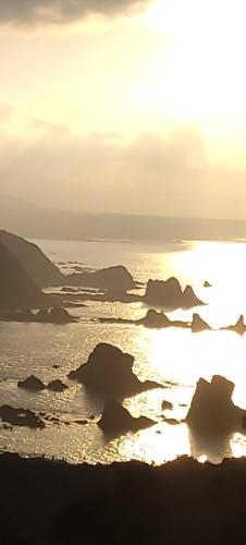 a sunset over the ocean with rocks in the water at Hotel Restaurante el Fornon in Novellana