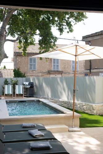 - une piscine avec un parasol, des chaises et une table dans l'établissement MAISON V AU COEUR DU VILLAGE Alpilles, à Maussane-les-Alpilles