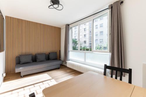 un salon avec un canapé et une grande fenêtre dans l'établissement Nouvel Appartement Cosy Montparnasse, à Paris