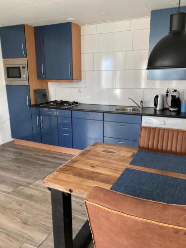 a kitchen with blue cabinets and a wooden table at Bungalow op bedrijf met melkkoeien in De Cocksdorp