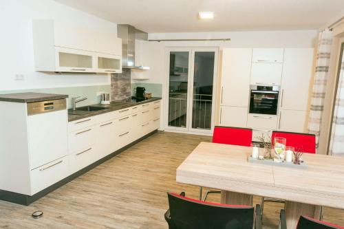 uma cozinha com armários brancos e uma mesa de madeira com cadeiras vermelhas em Ferienwohnung im Allgäu - Biber 2 em Leutkirch im Allgäu