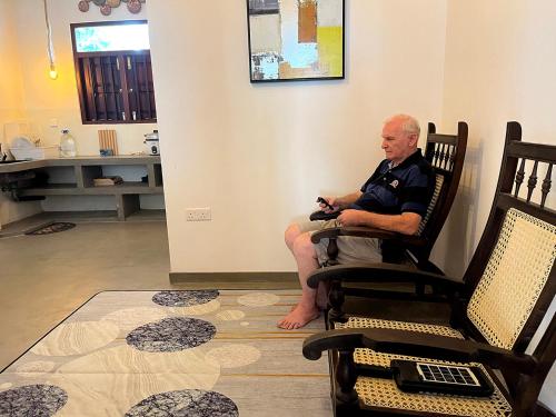 Ein älterer Mann sitzt auf einem Stuhl in einem Zimmer. in der Unterkunft Ceylon Little Paradise in Hikkaduwa