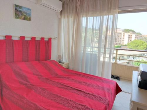 - un lit rouge dans une chambre avec une grande fenêtre dans l'établissement Bocca Baie T2 en bord de mer - Axelle Loc Appart, à Cannes
