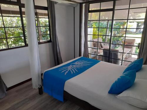 Fare Tetahora في Tevaitoa: غرفة نوم مع سرير مع الوسائد الزرقاء والنوافذ