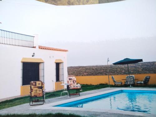 a swimming pool with chairs and an umbrella next to a house at CASA RURAL LA CABRA DEL MEDIO in Monesterio