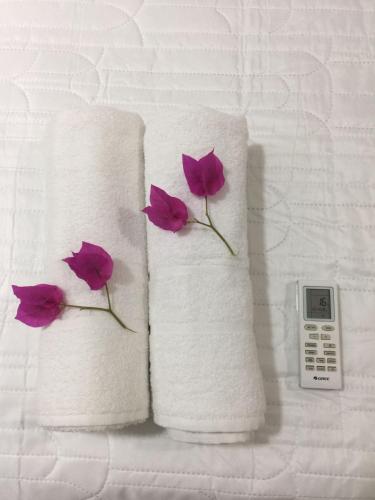 dos toallas con flores púrpuras junto a un mando a distancia en HOSTEL D´ SALLES (PRÓXIMO AO AEROPORTO), en Palmas