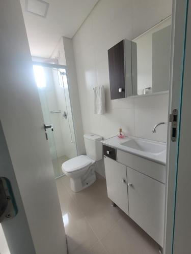 a white bathroom with a toilet and a sink at Sunset Itapema in Itapema