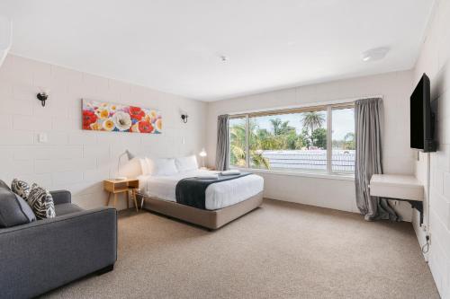 a bedroom with a bed and a couch and a window at Avalon Motel Thames - Wenzel Motels in Thames