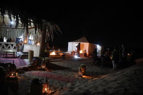 a group of people standing around a tent at night at Majorelle Desert Camp in Zagora