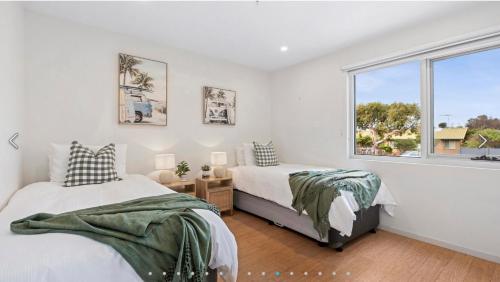 Dos camas en un dormitorio con ventana. en Ocean Grove Breeze On The Terrace Coastal Apartment, en Ocean Grove