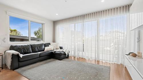 a living room with a black couch and a large window at Ocean Grove Breeze On The Terrace Coastal Apartment in Ocean Grove