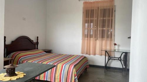 a bedroom with a bed and a table and a window at Chalé Arcos do Sol - Carrancas in Carrancas