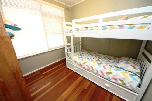a bedroom with two bunk beds and a window at Little Bay Cottage - 8 East Street Arakoon in Arakoon