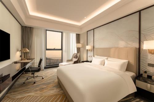 a bedroom with a large white bed and a desk at Grand New Century Hotel Binjiang Hangzhou in Hangzhou