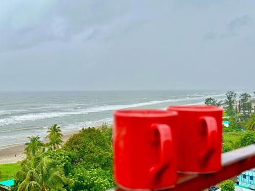 due tazze di caffè rosse sedute su un balcone che si affacciano sulla spiaggia di Modern Resort a Cox's Bazar