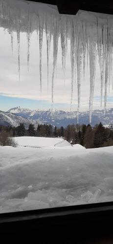 una ventana con carámbanos colgando sobre un campo cubierto de nieve en Appartamento a Francolini, en Folgaria