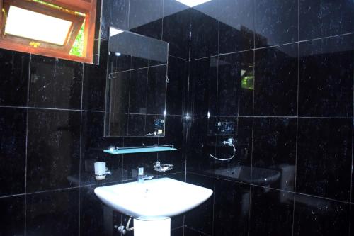 La salle de bains est pourvue de carrelage noir, d'un lavabo et d'un miroir. dans l'établissement Aramba Safari Resort, à Uda Walawe