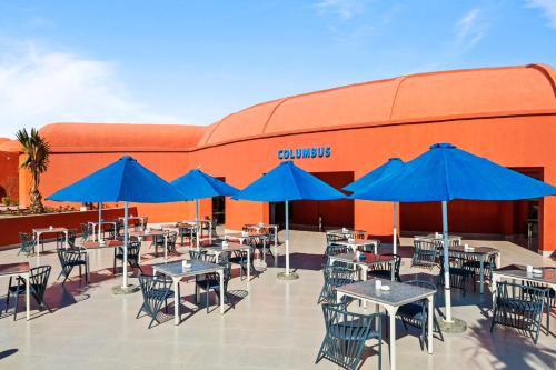 a patio with tables and blue umbrellas in front of a building at Pickalbatros Laguna Club Resort Sharm El Sheikh in Sharm El Sheikh