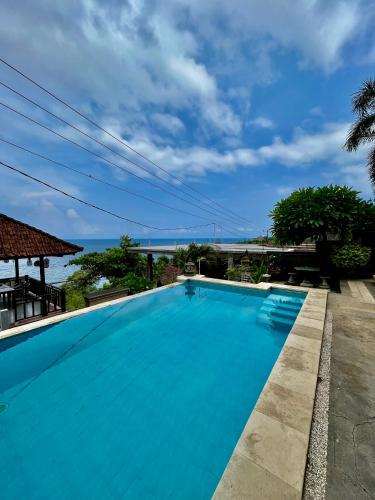 a large blue swimming pool with a view of the ocean at Acarya Bungalows in Ambat