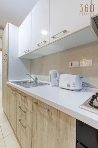 a kitchen with white cabinets and a sink at Modern 1BR home with Private Balcony in St Julians by 360 Estates in Tal-Għoqod