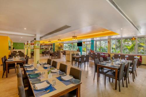 a restaurant with wooden tables and chairs and windows at Sterling Goa Varca in Varca