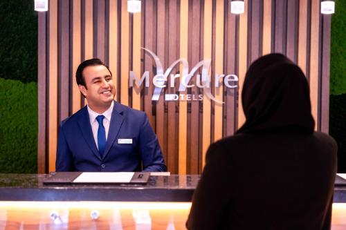 a man in a suit and tie sitting at a table with a laptop at Mercure Dubai Barsha Heights Hotel Suites And Apartments in Dubai