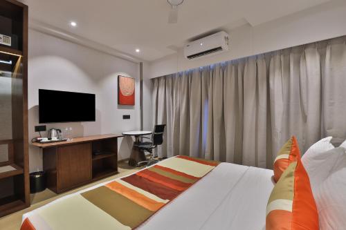 a hotel room with a bed and a desk with a television at Hotel Elements Surat in Surat