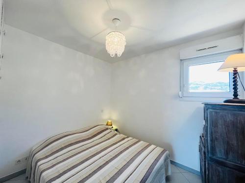 une chambre avec un lit, une fenêtre et un lustre dans l'établissement Appartement 19 Les Carolines 2 Calvi, à Calvi