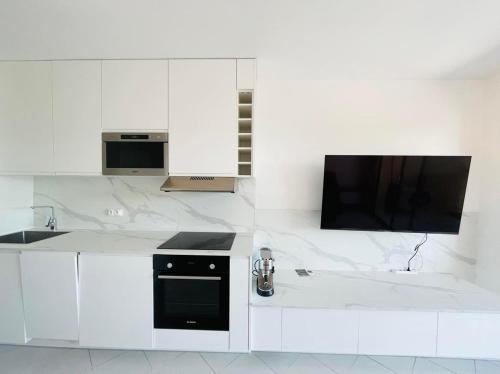 une cuisine blanche avec cuisinière et télévision dans l'établissement Appartement 19 Les Carolines 2 Calvi, à Calvi