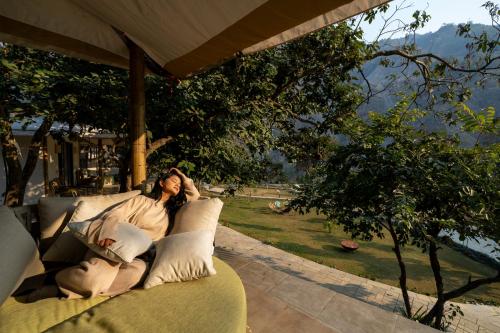 a woman sitting on a couch on a patio at ONENESS Rishikesh by Ganga Kinare - A Luxury Wilderness Resort in Rishīkesh