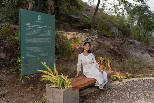 a woman sitting on a bench next to a sign at ONENESS Rishikesh by Ganga Kinare - A Luxury Wilderness Resort in Rishīkesh