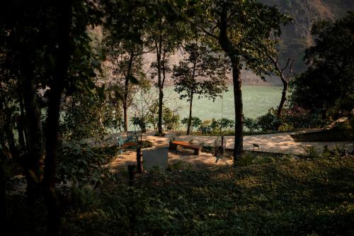 a park with a bench and a body of water at ONENESS Rishikesh by Ganga Kinare - A Luxury Wilderness Resort in Rishīkesh
