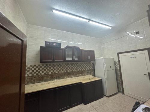 La cuisine est équipée de placards bruns et d'un réfrigérateur blanc. dans l'établissement شقه للأيجار في الحي الشرقي, à Irbid