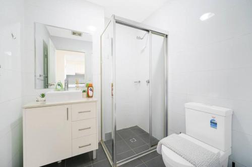 a white bathroom with a shower and a toilet at Shyline Views - Beautiful Condo In Wolli Creek in Sydney