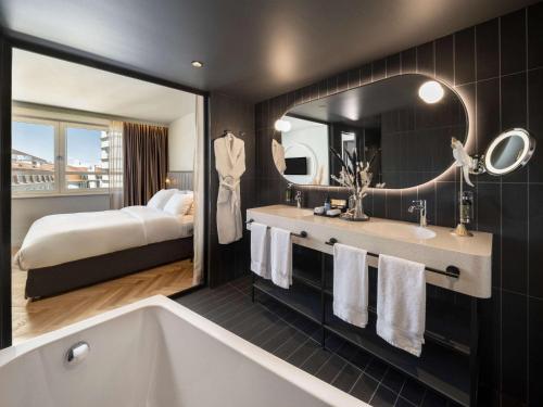 baño del hotel con bañera y cama en Hotel Am Konzerthaus Vienna - MGallery en Viena