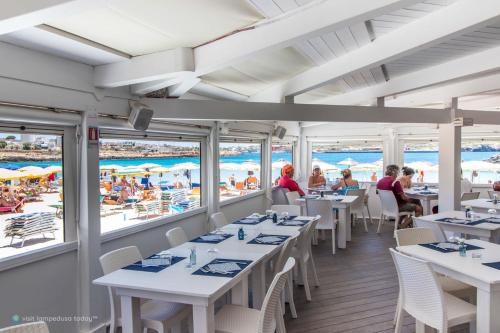 un ristorante con tavoli e sedie bianchi e la spiaggia di Hotel Guitgia Tommasino a Lampedusa