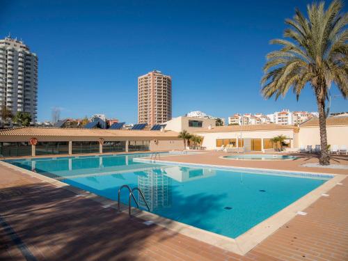 a large swimming pool with palm trees and buildings at Praia da Rocha Beach Retreat in Portimão