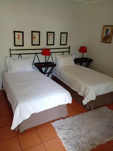 2 letti con lenzuola bianche e lampade rosse in una stanza di HLULALA GUEST HOUSE a Hluhluwe