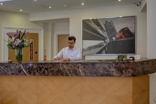 a man standing behind a counter in a hotel lobby at Queensway Hotel, Sure Hotel Collection by Best Western in London