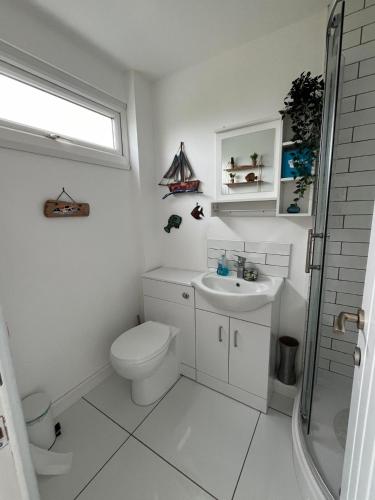 a white bathroom with a toilet and a sink at 288, Two bed Chalet on Belle Aire Holiday Park - With private veranda, sleeps 5, pet friendly, free Wi-Fi, bed linen and towels included and onsite entertainment available in Hemsby