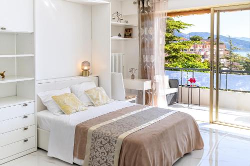 une chambre blanche avec un lit et une grande fenêtre dans l'établissement Magnifique studio limitrophe Monaco, parking privé, à Roquebrune-Cap-Martin