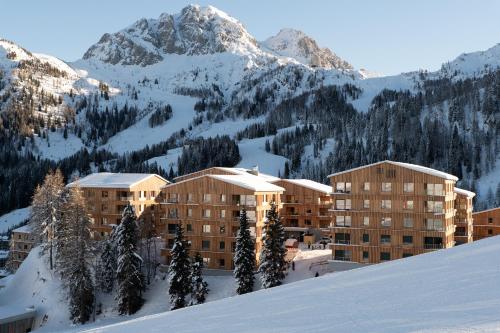 un edificio en la nieve con una montaña en el fondo en Wohnfühl-Apartment "Bergkristall 08" im Almresort Sonnenalpe Nassfeld, en Hermagor