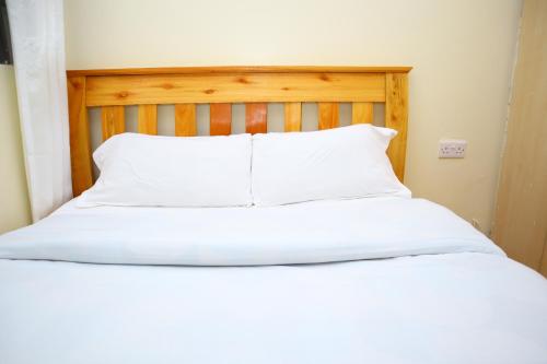 a bed with white sheets and a wooden headboard at SAGE Apartments-South B in Nairobi