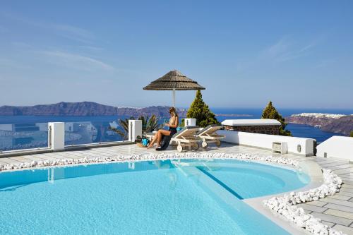 Eine Frau, die unter einem Regenschirm neben einem Pool sitzt. in der Unterkunft Santorini Princess Spa Hotel in Imerovigli