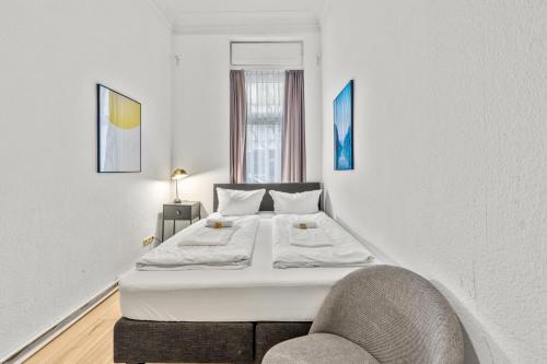 a white bedroom with a bed and a chair at primeflats - Apartment Leberstr 58 Berlin Schöneberg in Berlin